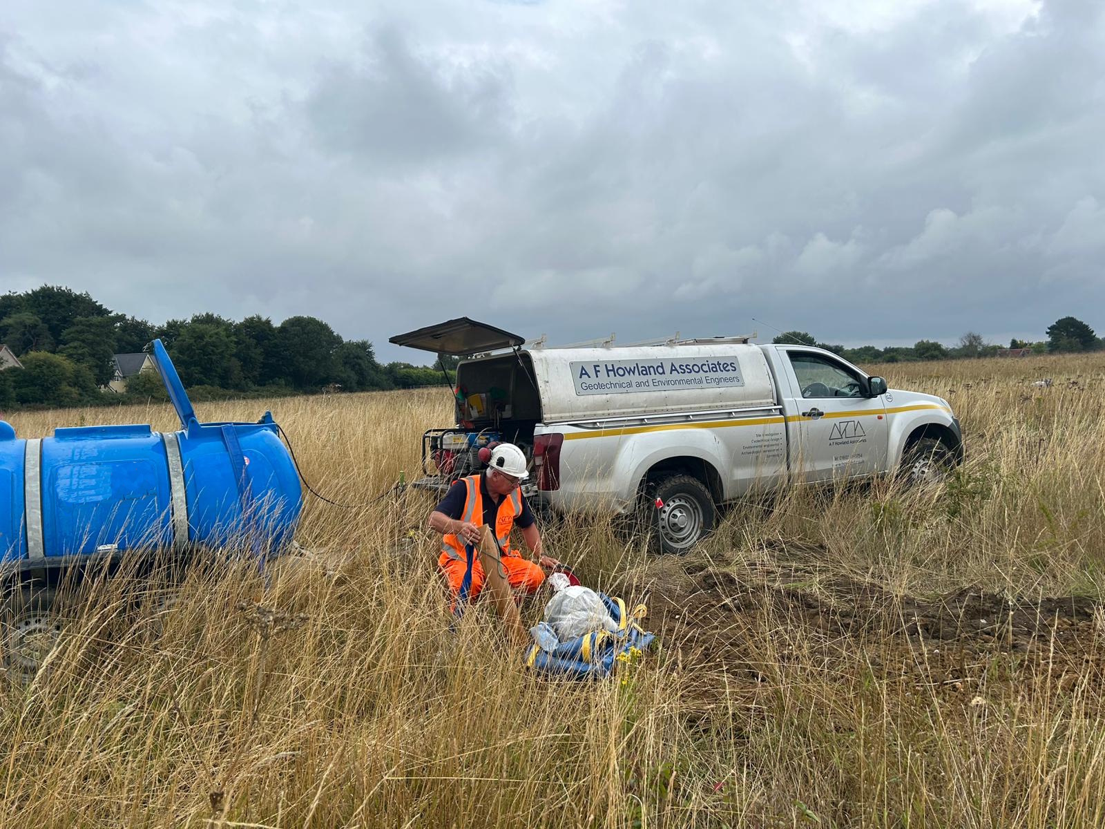 Technician conducting soakaway testing beside A F Howland Associates vehicle in a rural field.